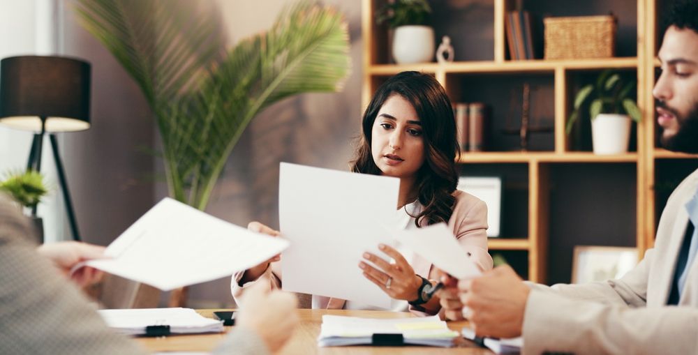 Business meeting: woman examining papers, focused, seated with colleagues in an office.