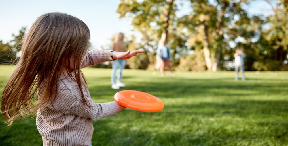 Girl throwing a frisbee in a park, with friends in the background.