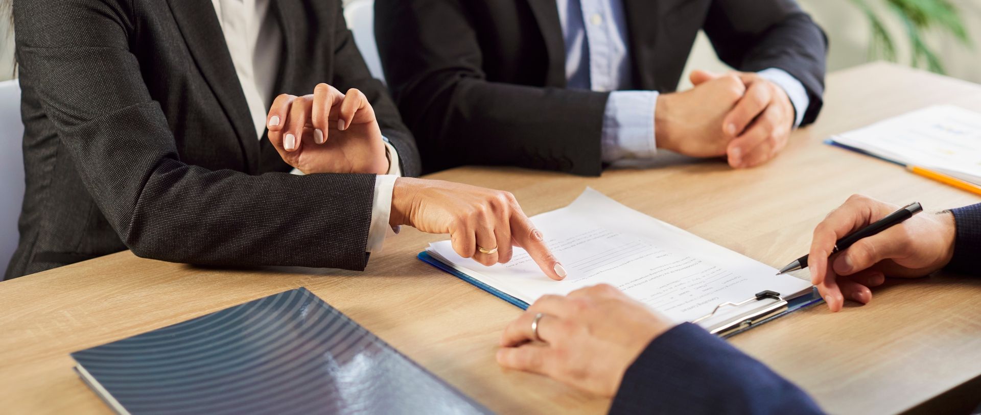People in suits reviewing and signing a document at a table.