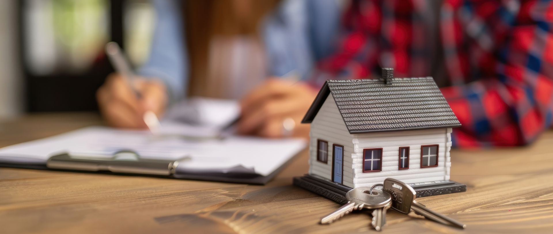 A couple signing paperwork for a house with a model house and keys on a table.