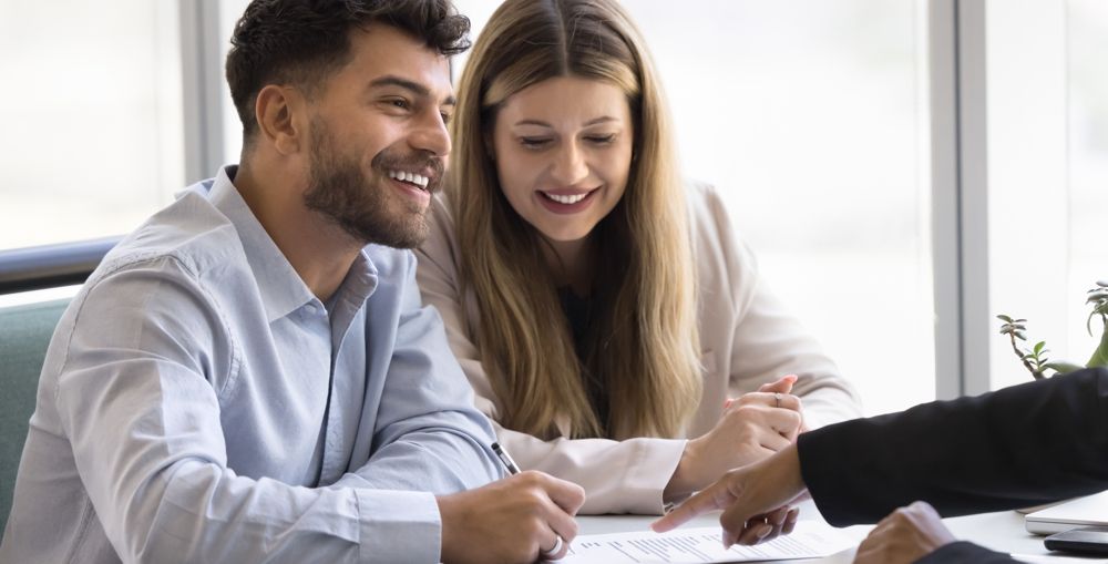 Couple smiling, reviewing documents with someone in an office setting.
