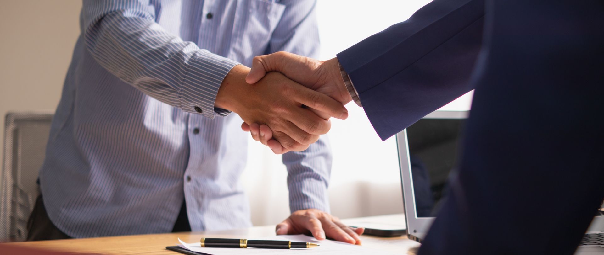 Two people shaking hands over a table, possibly sealing a business deal.
