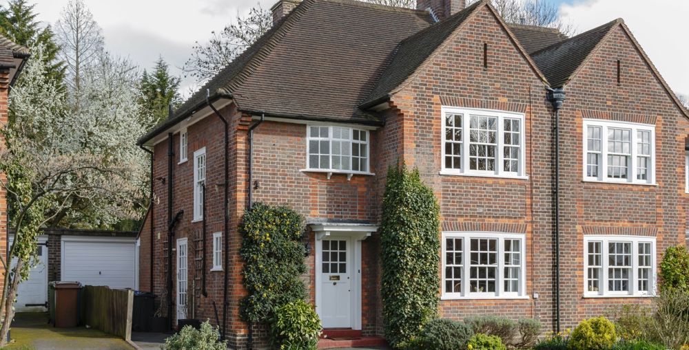 Brick house with white windows and door, surrounded by greenery.