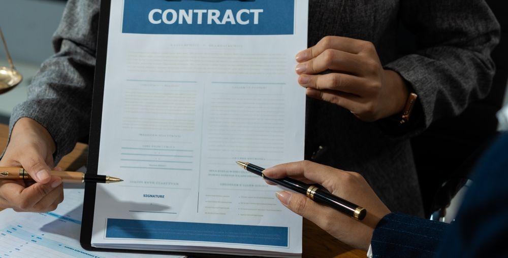 Person holding a contract, pointing a pen. Another person is also pointing at the contract. Legal setting.