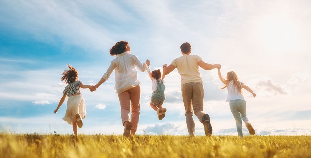 Family of five running through a field of gold, holding hands, sunny sky.