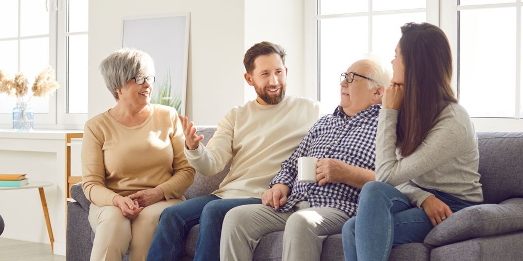 Family of four sits on a couch, talking. A woman is looking thoughtful.