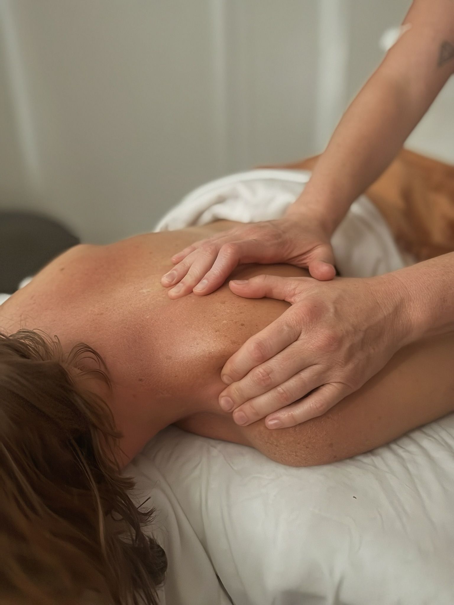 Person receiving a back massage with hands applying pressure on the shoulder, laying on a massage table.