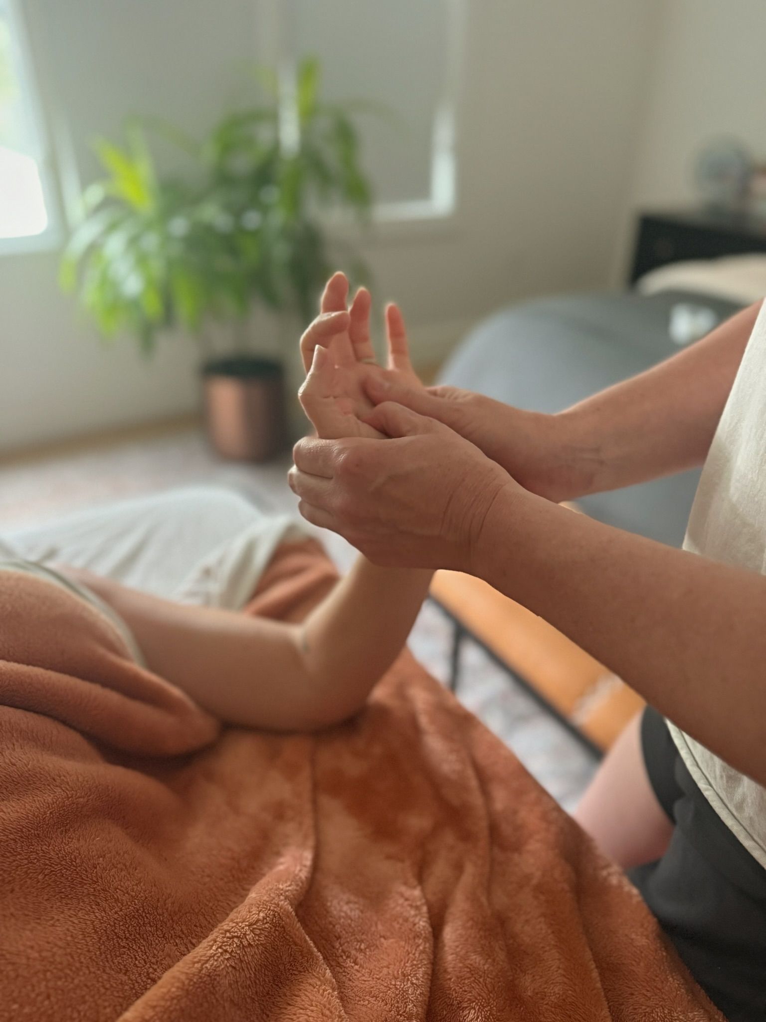 Hands receiving a massage. Therapist holds patient's forearm and hand on an orange towel. Interior setting.