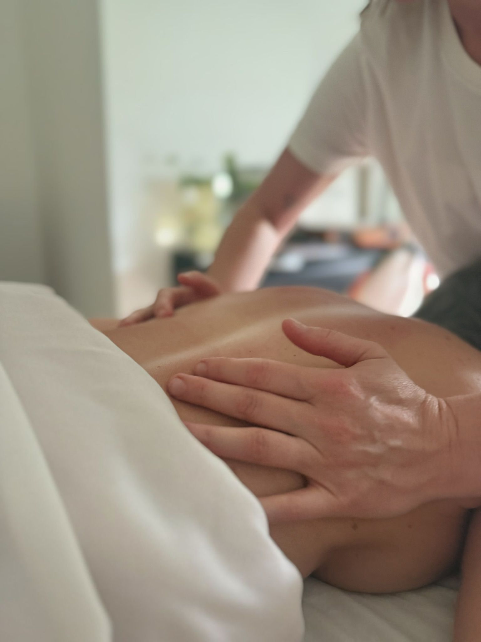 Hands giving a massage to a person's back in a room with white sheets.