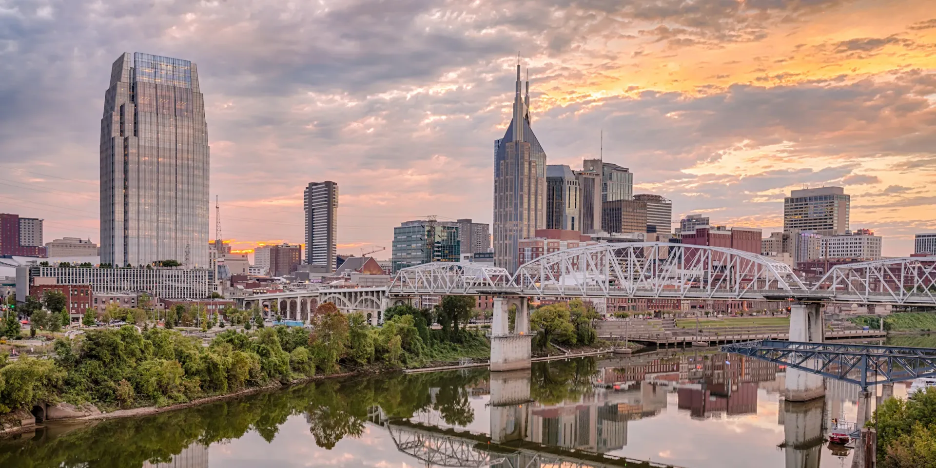 Nashville skyline with Cumberland River, bridge, and buildings at sunset.