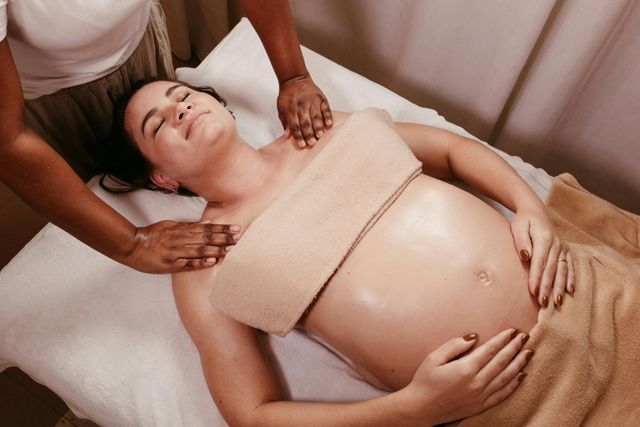 Pregnant woman receiving massage on a spa bed; her eyes are closed.
