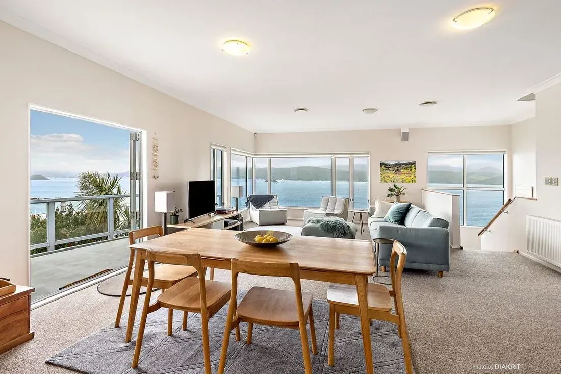 Bright coastal living room with dining table, gray sofa, large windows, and ocean view
