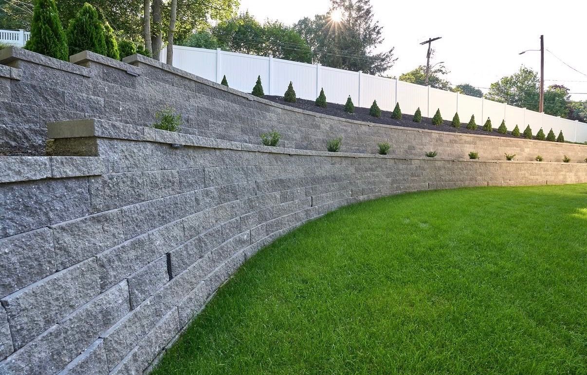 Curved gray stone retaining wall beside a bright green lawn and trees