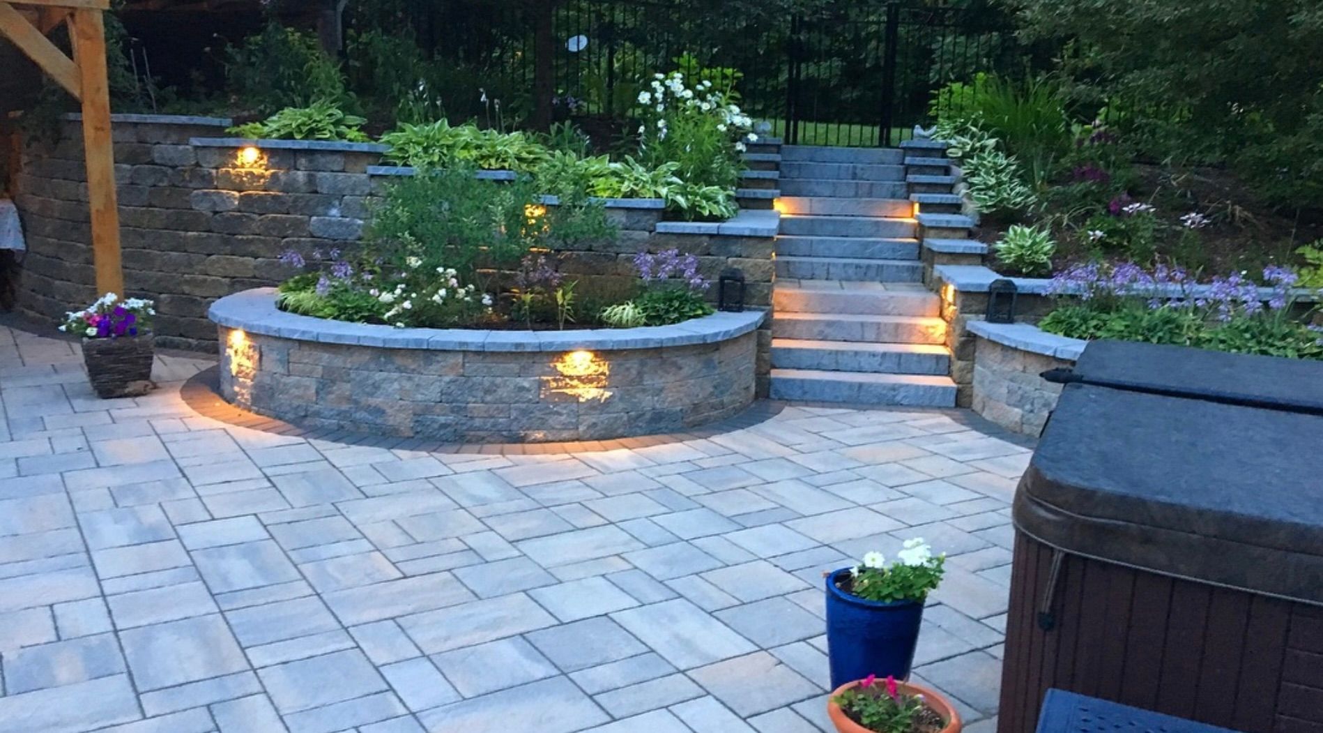 Stone patio with curved retaining wall, steps, and warm landscape lighting in a garden at dusk