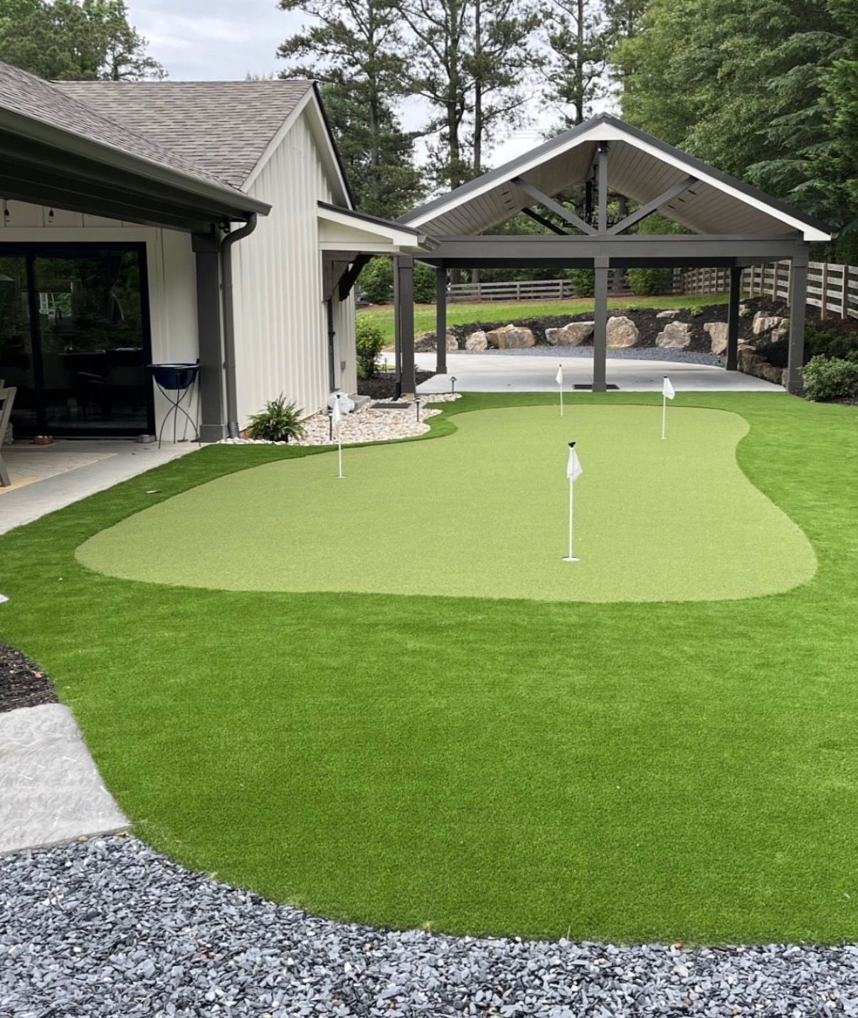 Backyard putting green beside a house, with white flags and a covered patio.
