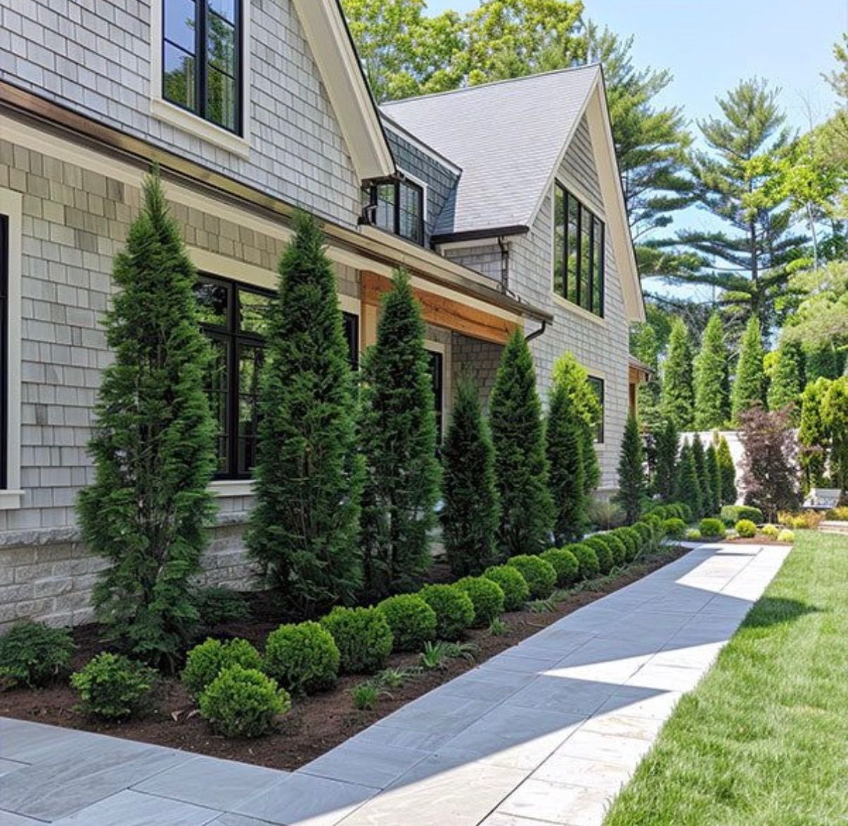 Modern house exterior with stone siding, tall evergreen shrubs, and a stone walkway along a manicured lawn