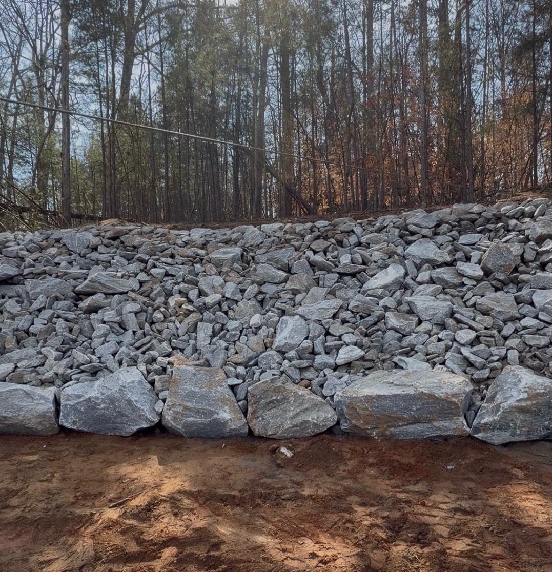 Rip Rap with woods behind it and bare soil in the foreground