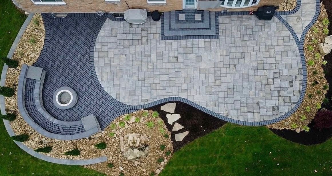 Curved stone patio beside a lawn with a small circular water feature and stepping stones.