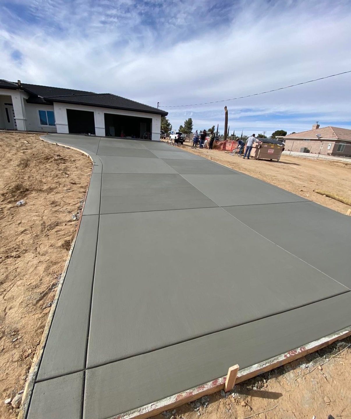 New concrete driveway leading to a house under construction on a dirt lot