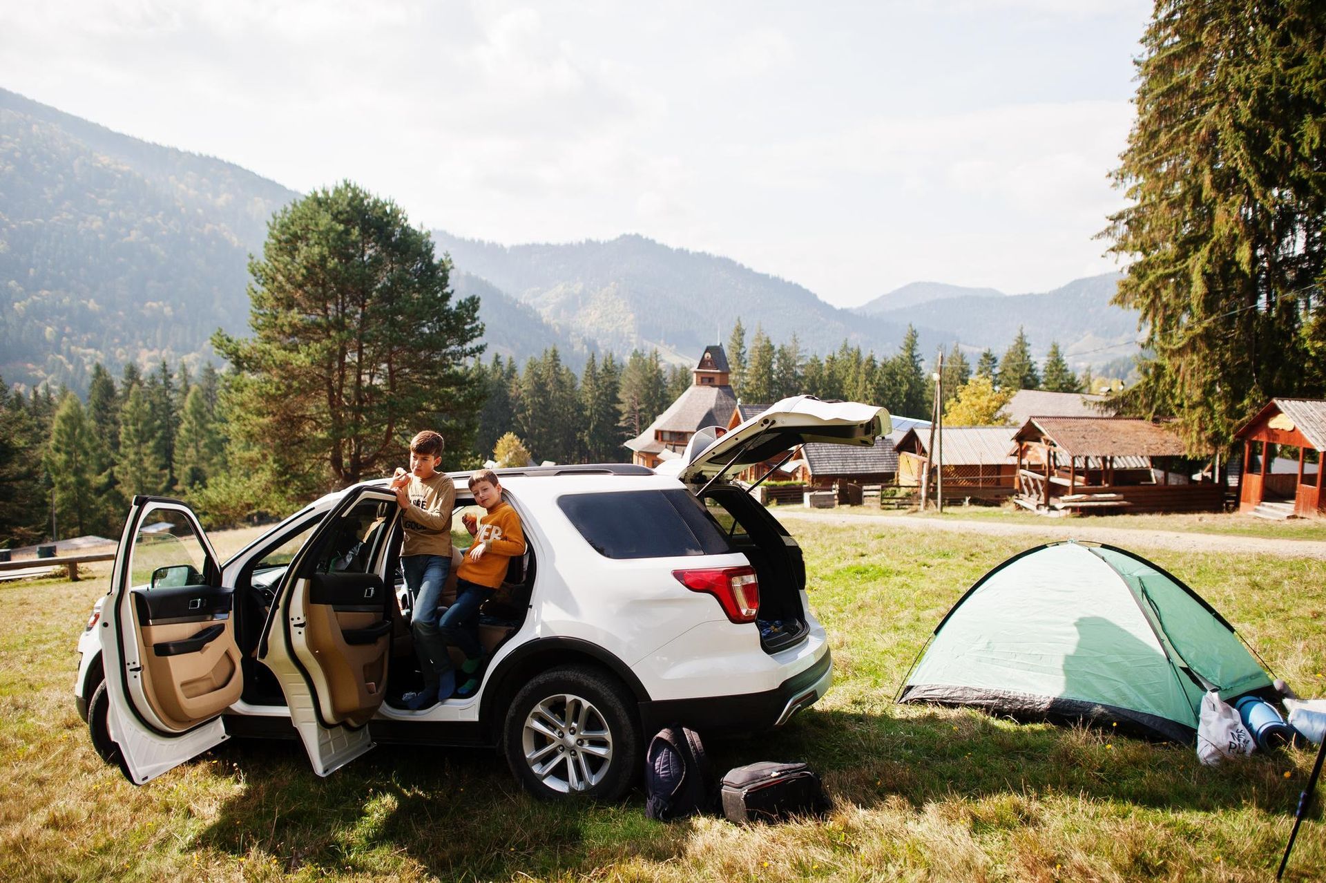 Family unloading gear from a white SUV next to a tent in a mountain campsite.