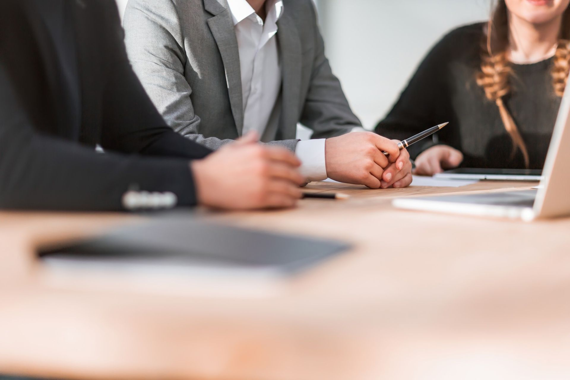 People in business attire at a table, discussing documents near a laptop.