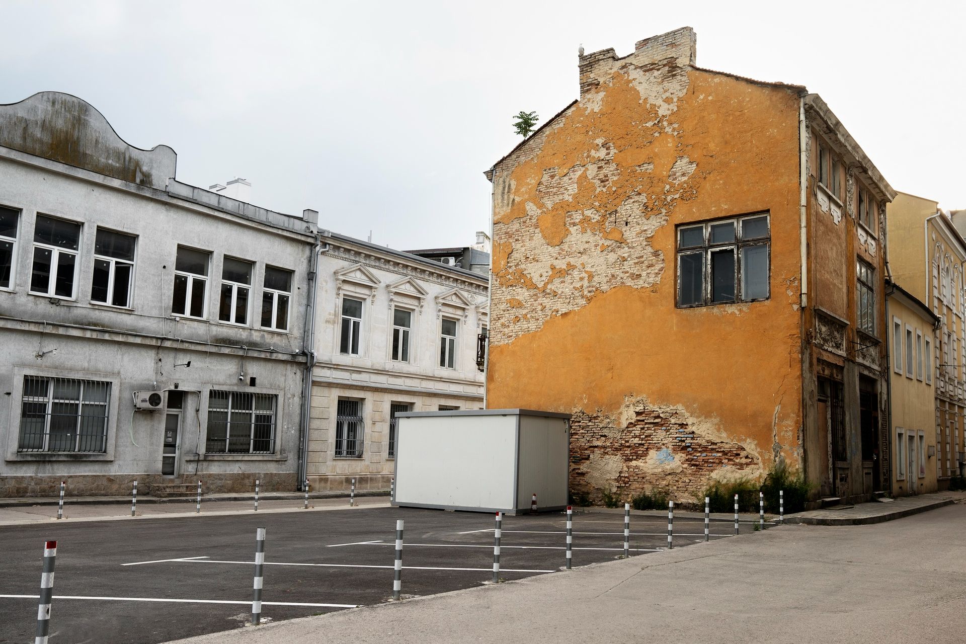 Buildings in varying states of repair, the main one being orange with peeling paint. A white storage unit sits out front.