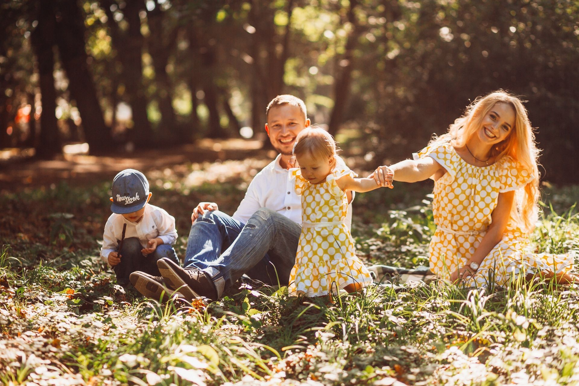 Family of four smiling, sitting in a sunny park with leaves on the ground.