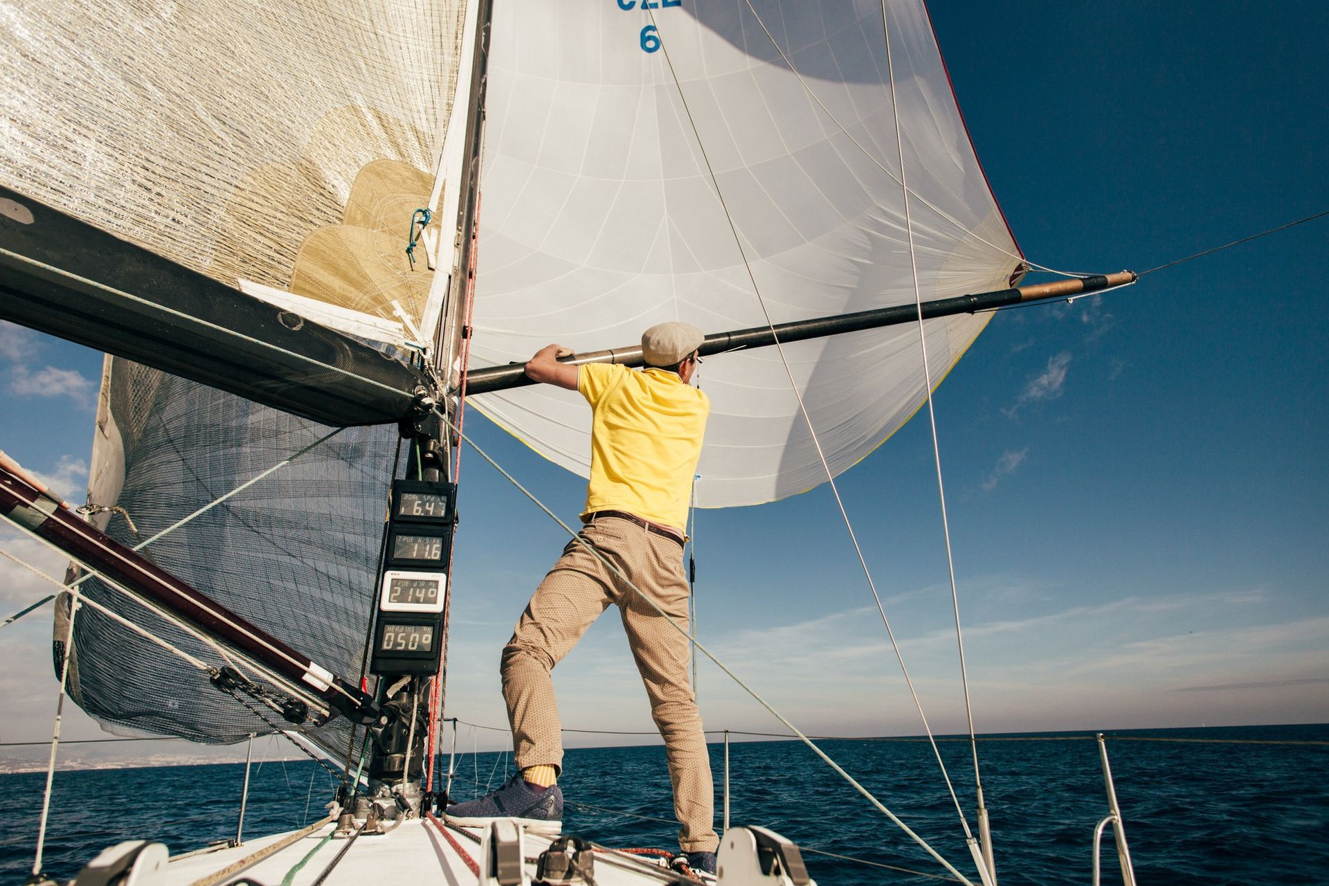 Man in yellow shirt on sailboat, adjusting the sail on a sunny day.