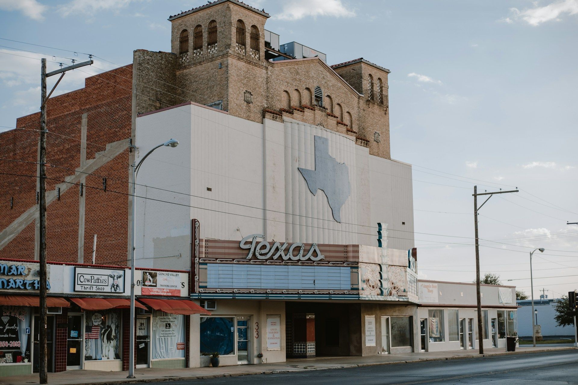 The Texas Theatre, white and tan facade with Texas-shaped emblem, marquee, and adjacent shops.