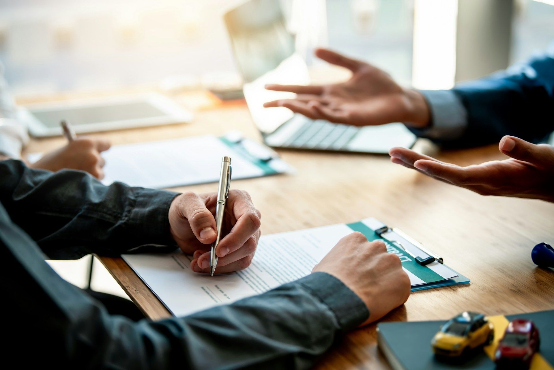People signing paperwork at a table; another person gestures with hands.
