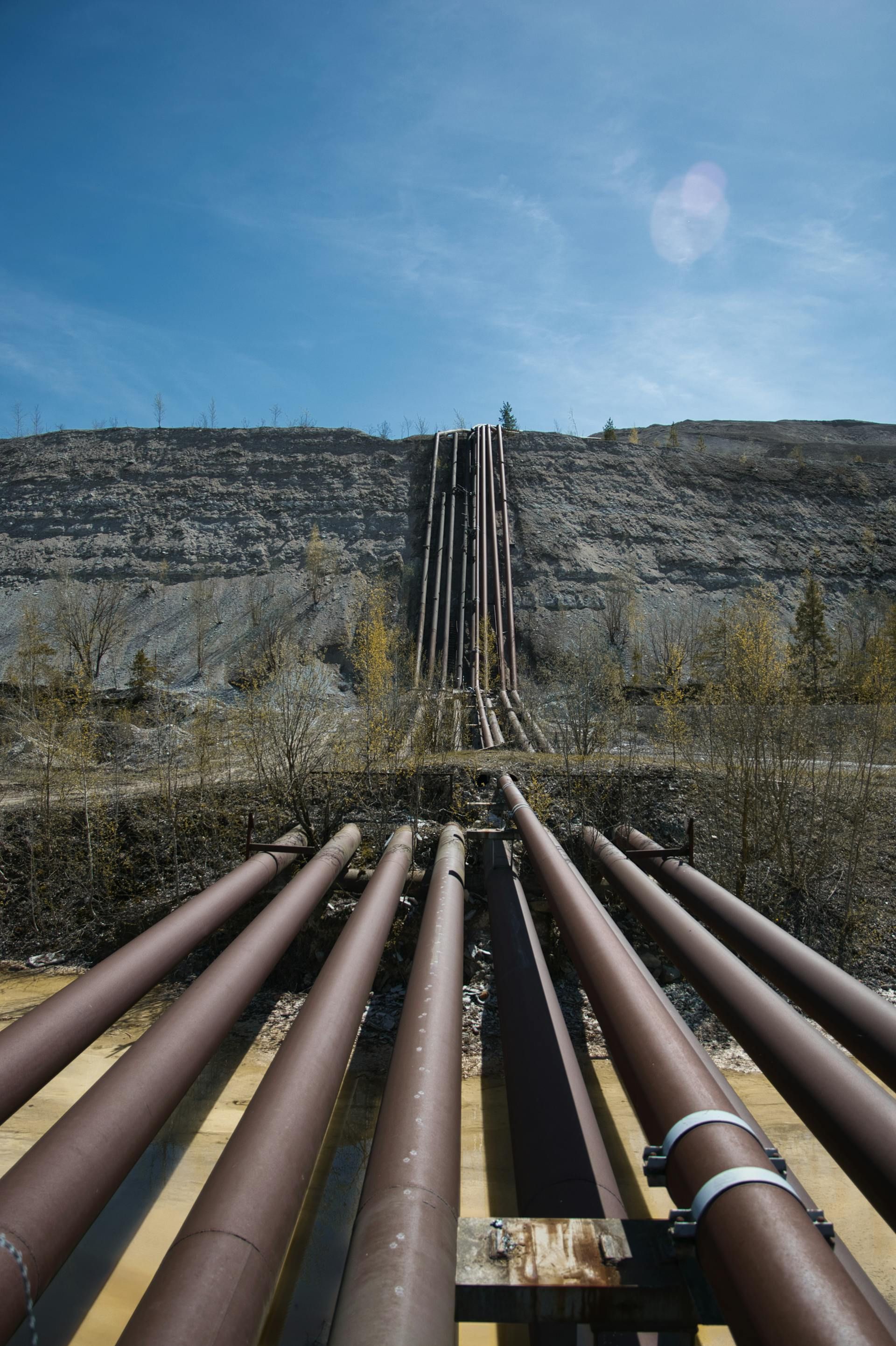 Brown pipes ascend a gray hillside against a blue sky.