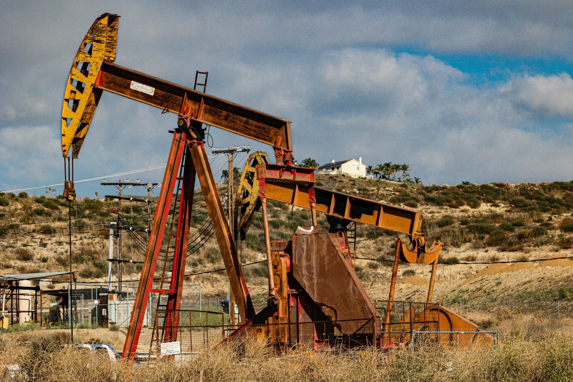 Two yellow and red oil pump jacks in a dry, grassy field, under a partly cloudy sky.