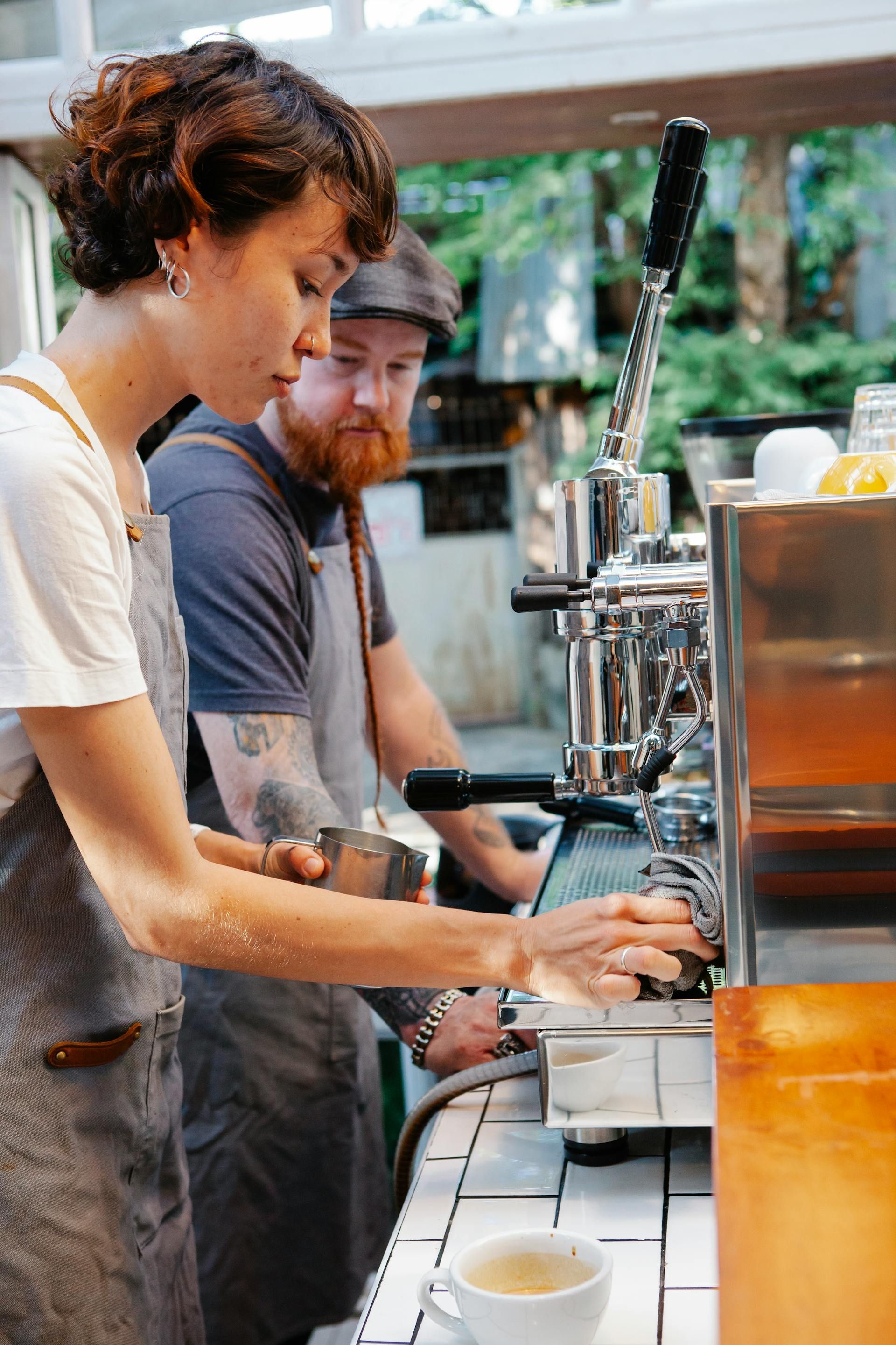 Two baristas making coffee with an espresso machine in a cafe.