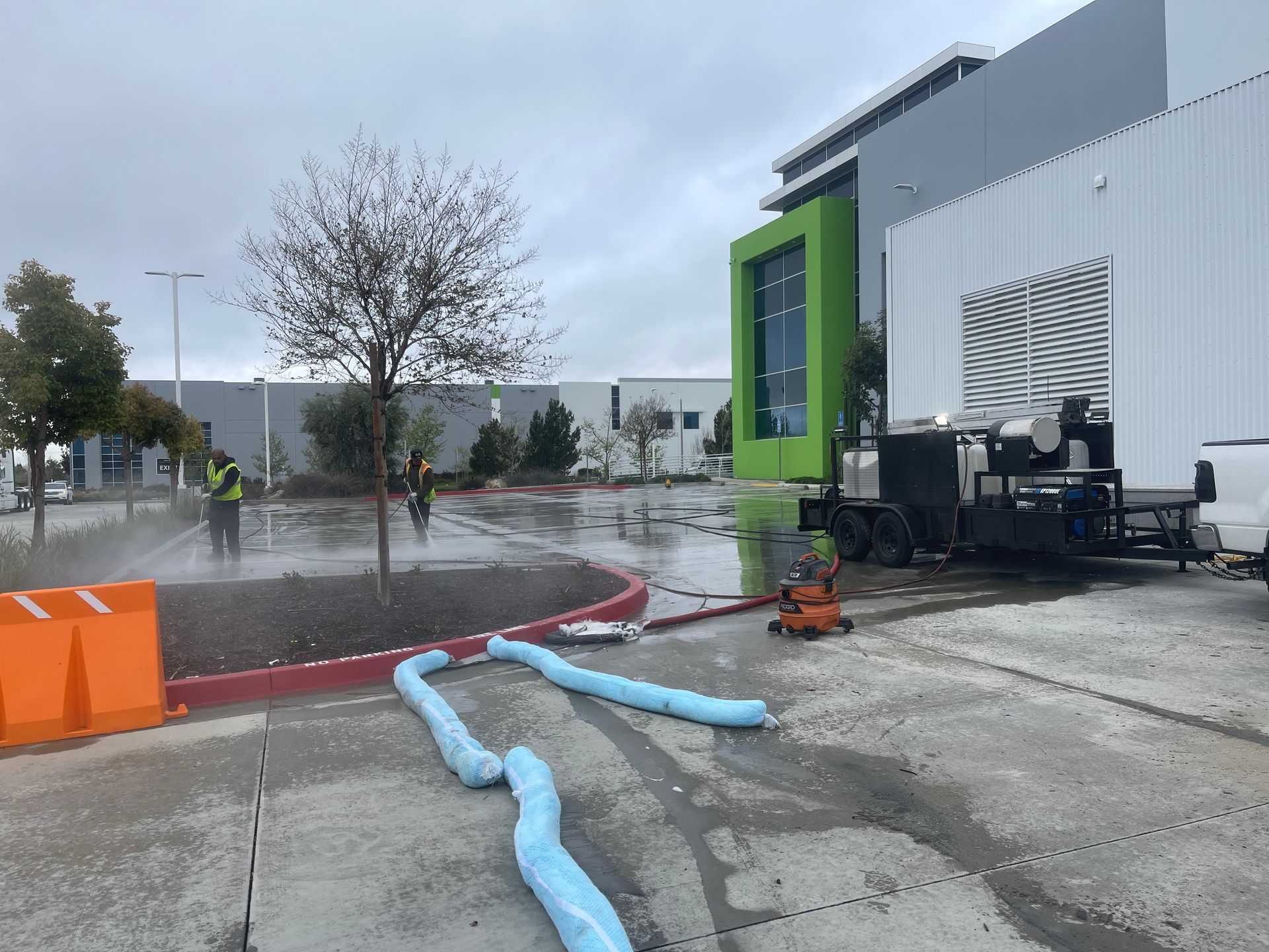 A man is spraying water on a sidewalk in front of a building.