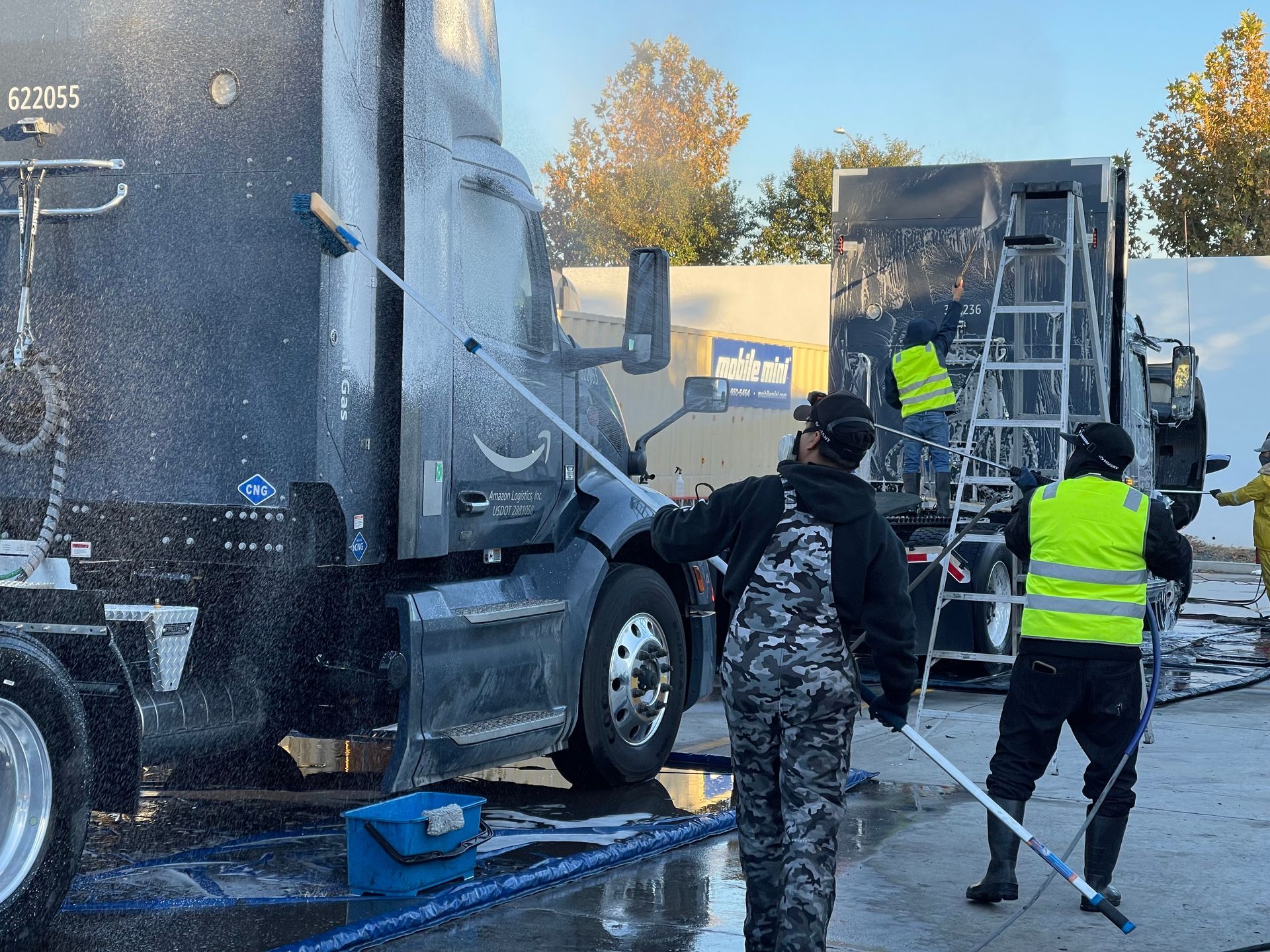 A group of people are washing a semi truck in a parking lot.