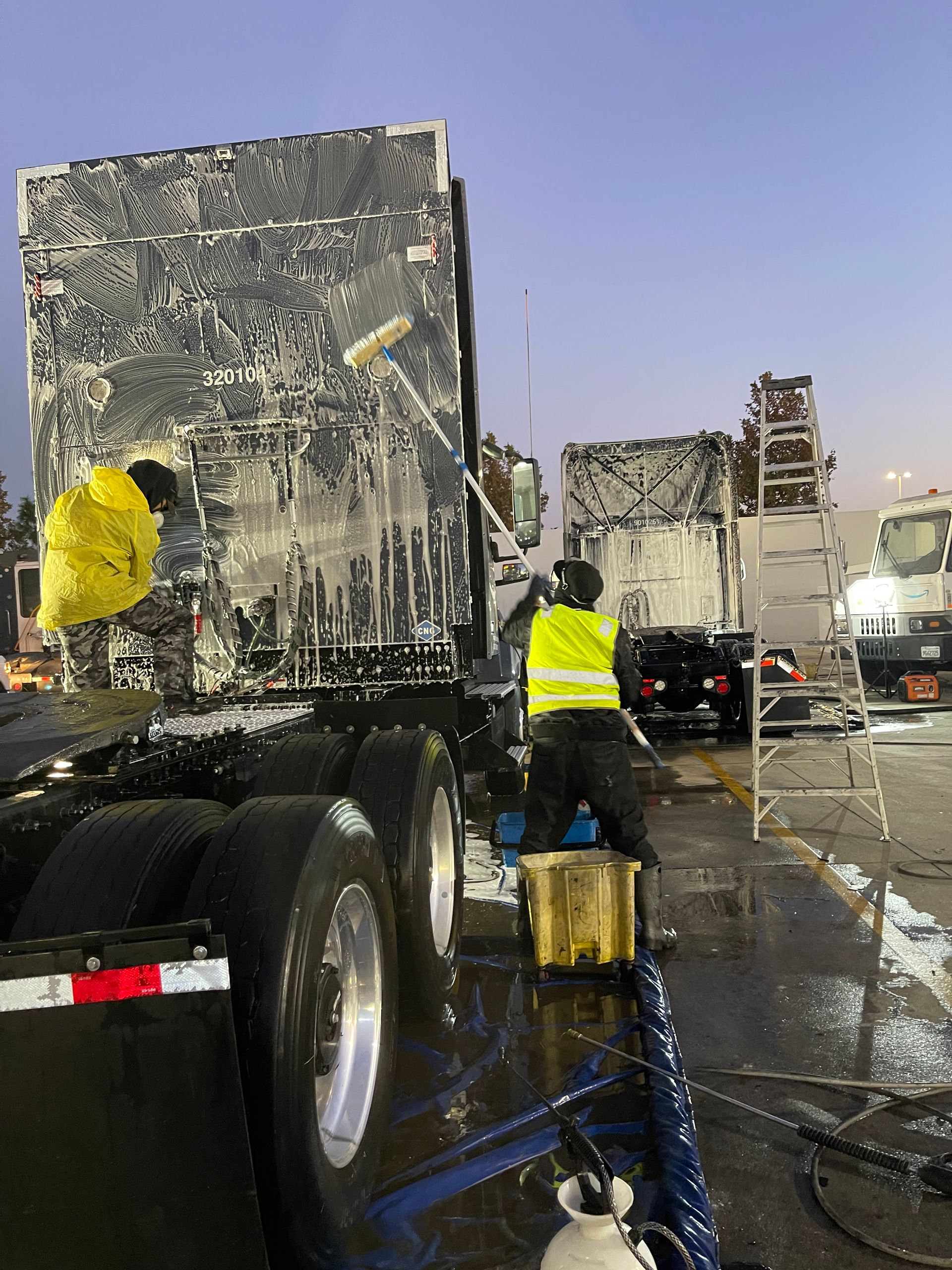 A man in a yellow vest is washing a truck.