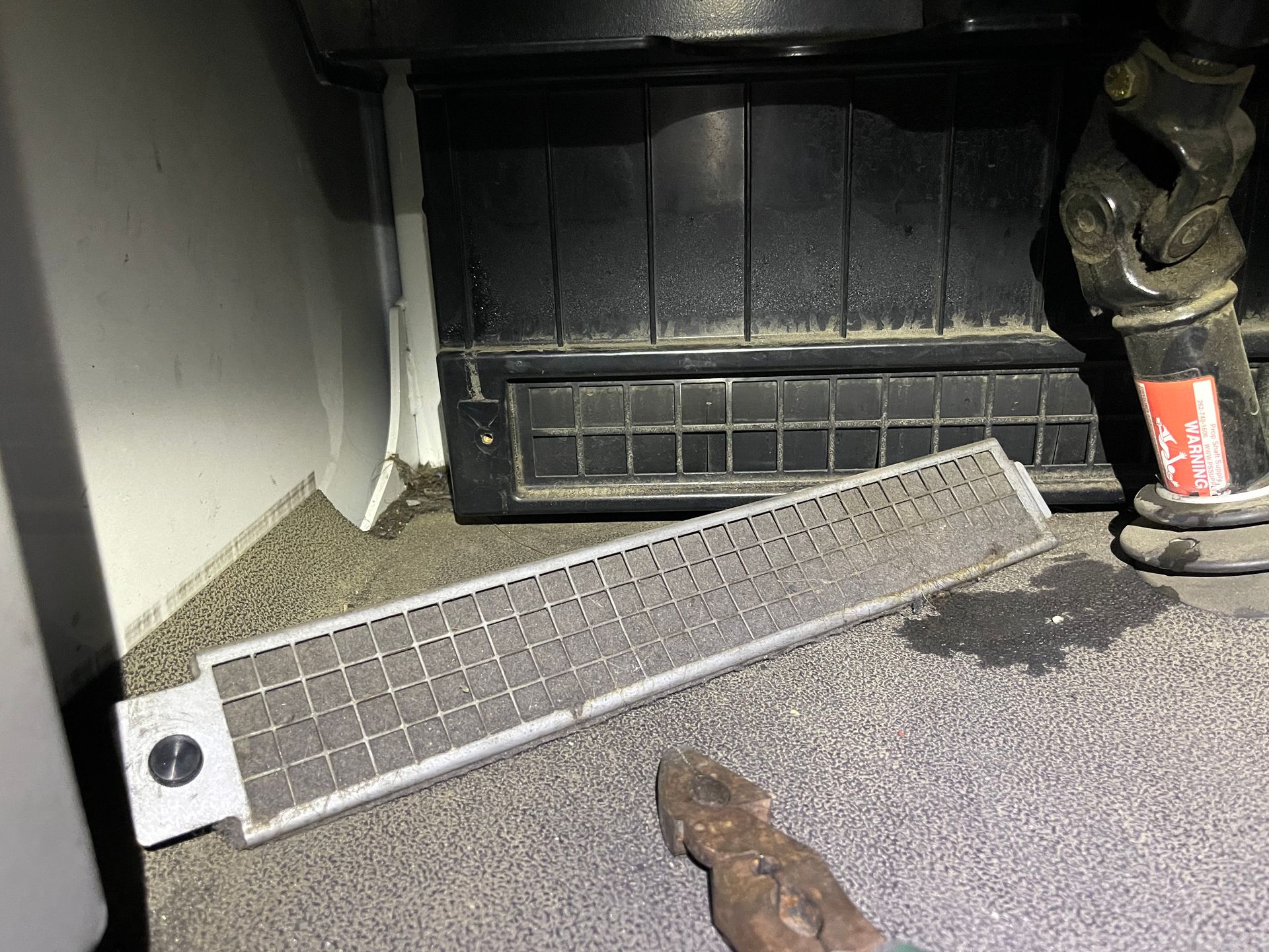 A piece of metal is laying on the floor next to a dirty air filter.