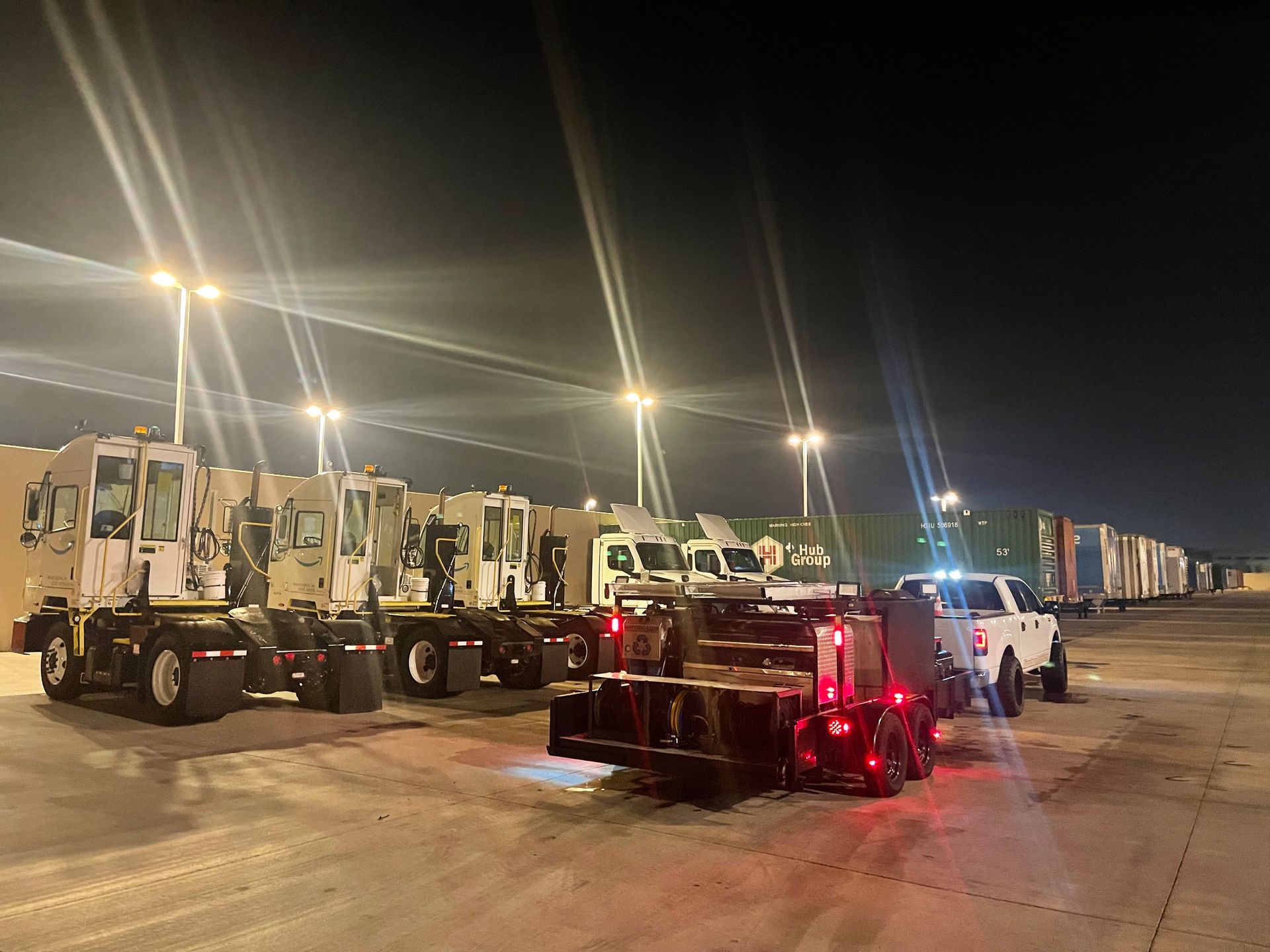 A row of trucks are parked in a parking lot at night.
