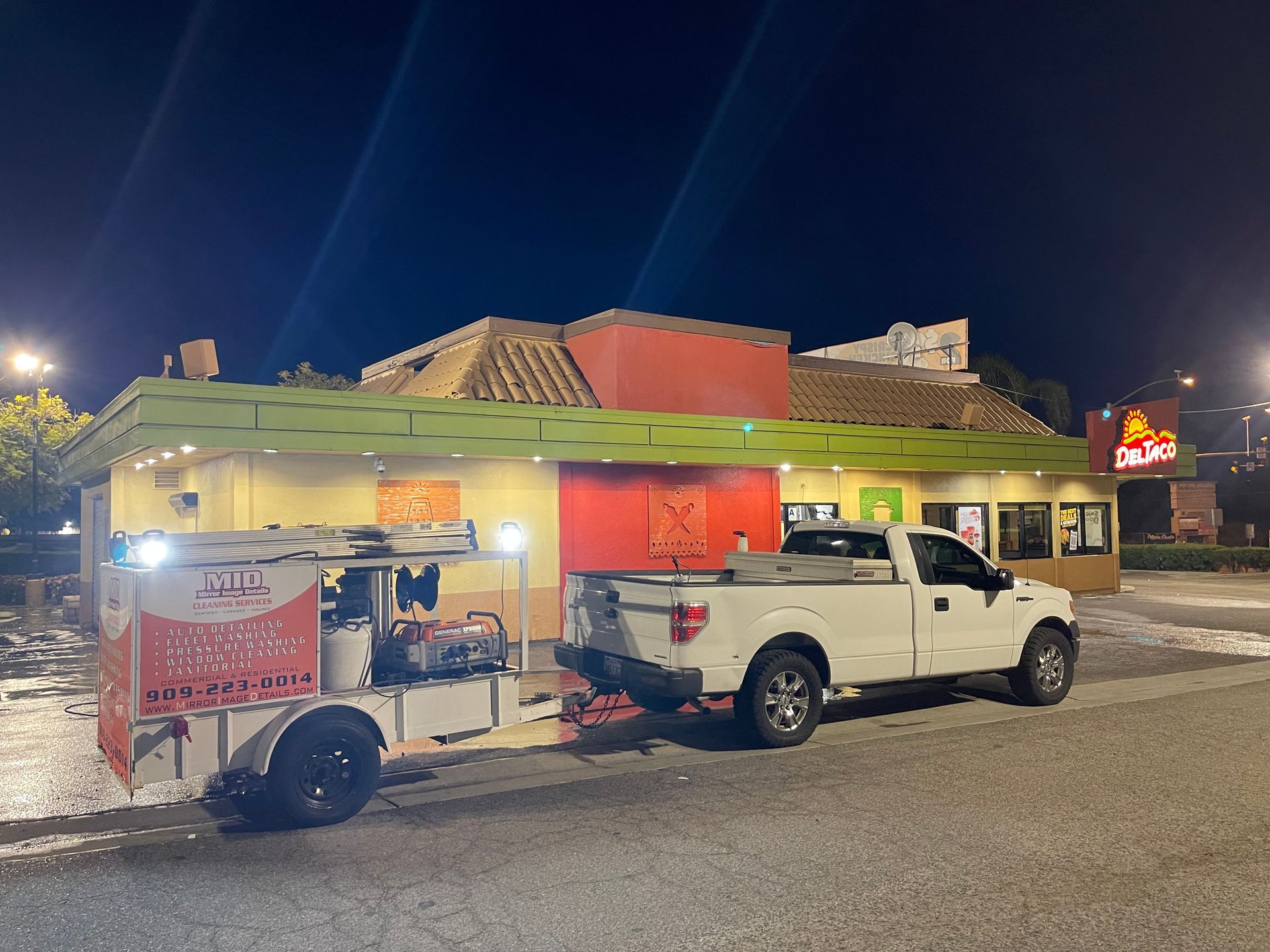 A white truck is parked in front of a restaurant at night.