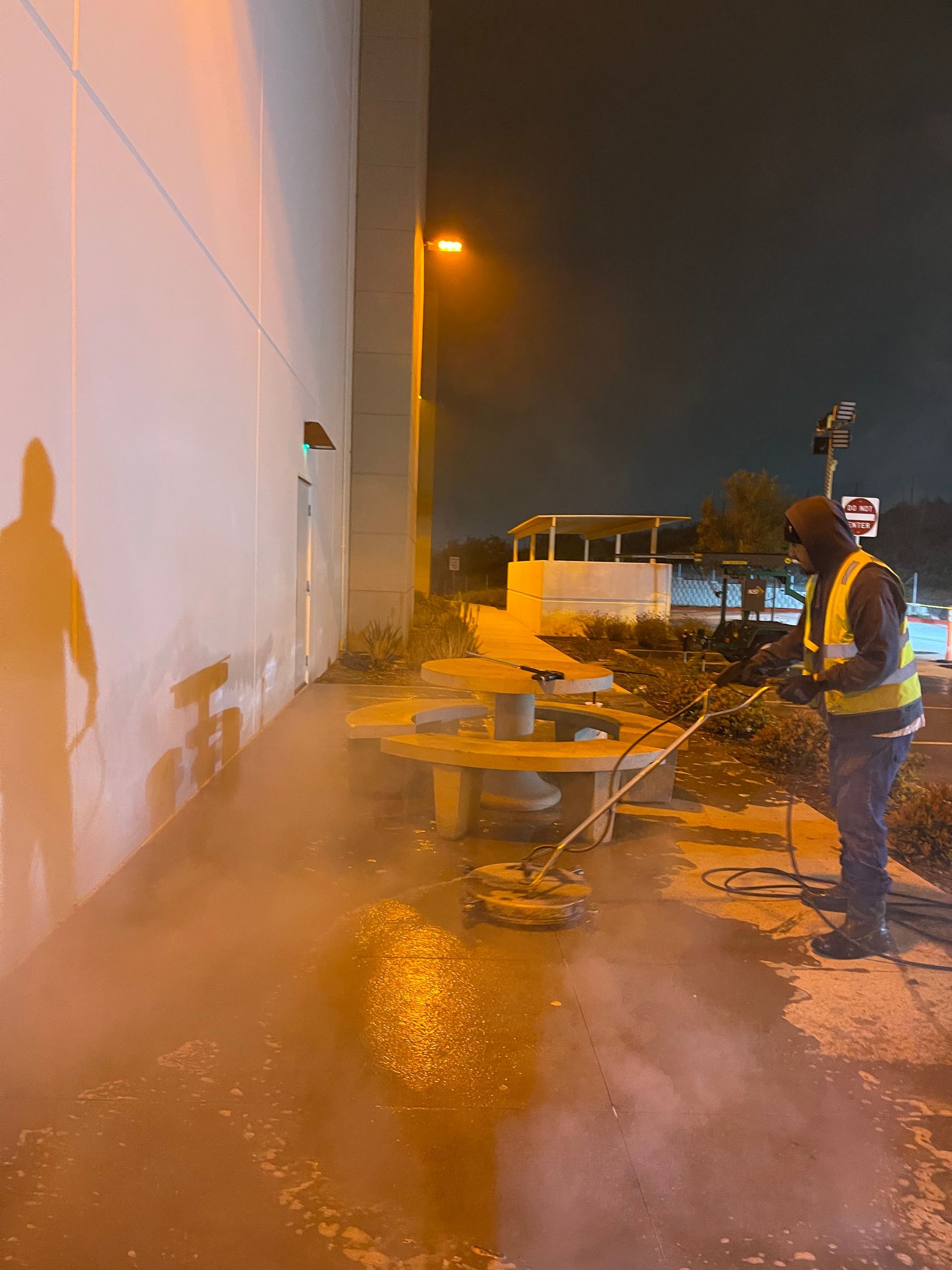 A man is cleaning the sidewalk outside of a building at night.