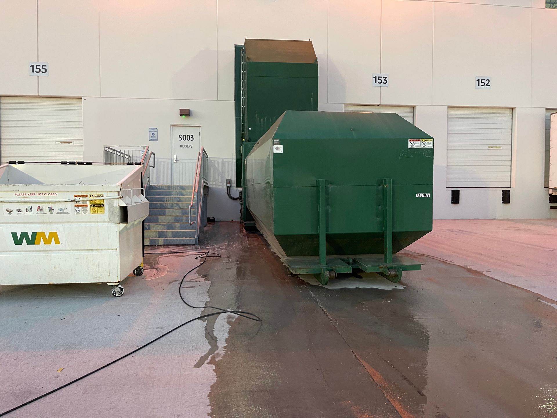 A green dumpster is sitting next to a white dumpster in a warehouse.