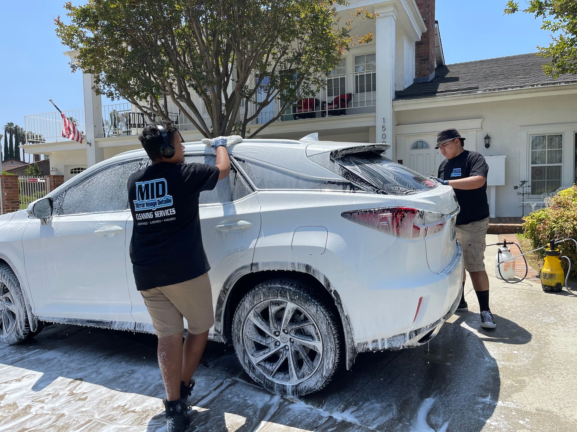 Two men are washing a white car in front of a house.