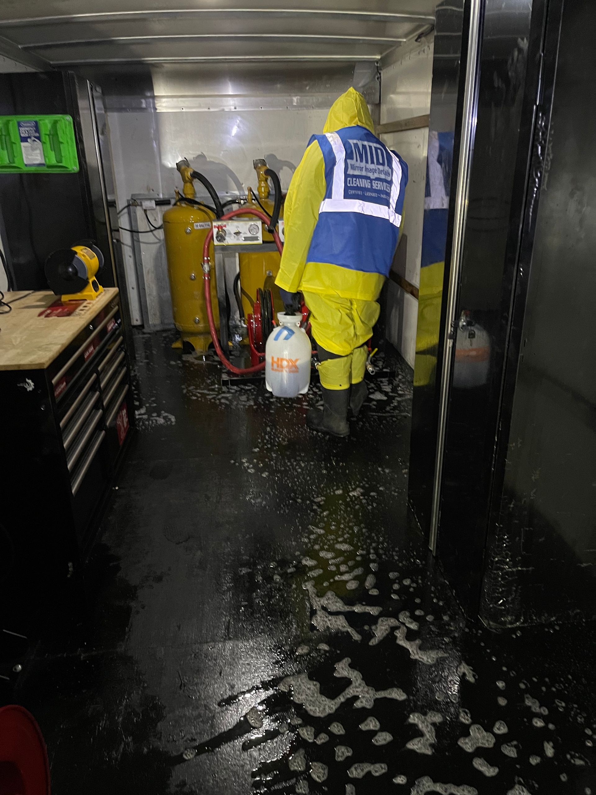 A man in a yellow and blue safety vest is spraying something in a room.