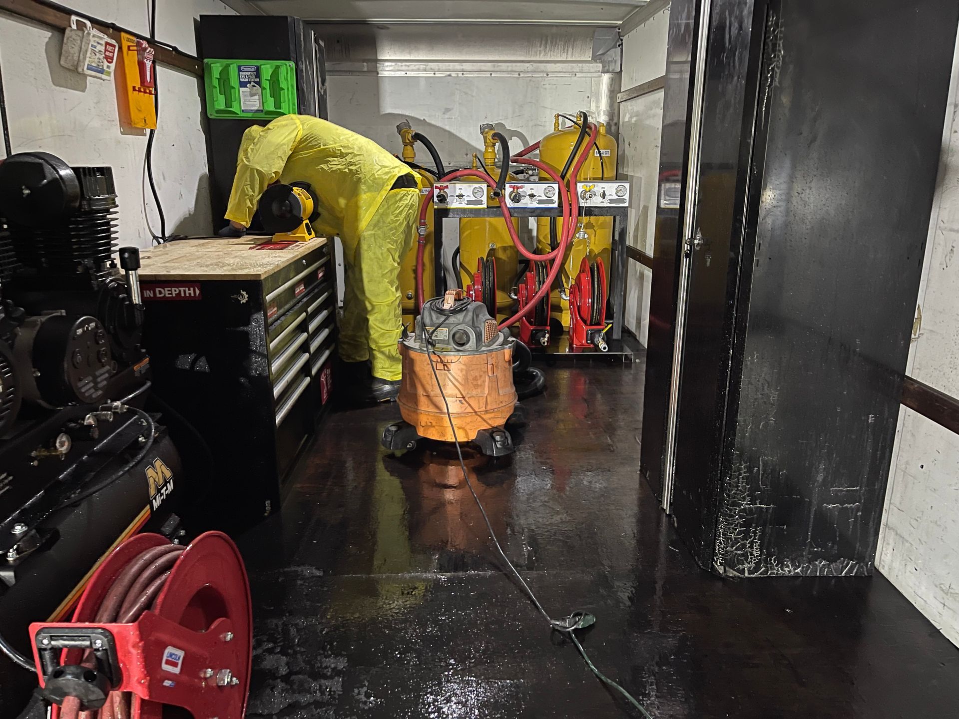 A man in a yellow suit is working on a machine in a trailer.
