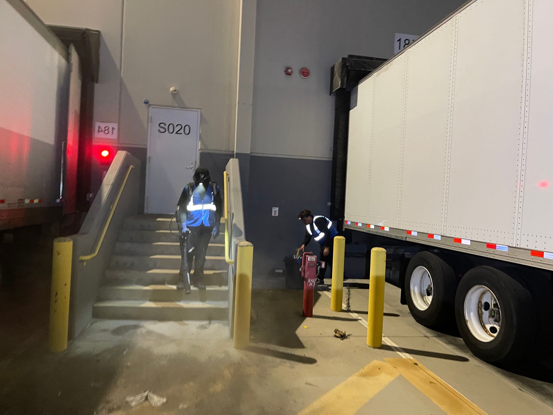A man is walking up stairs next to a truck in a warehouse.