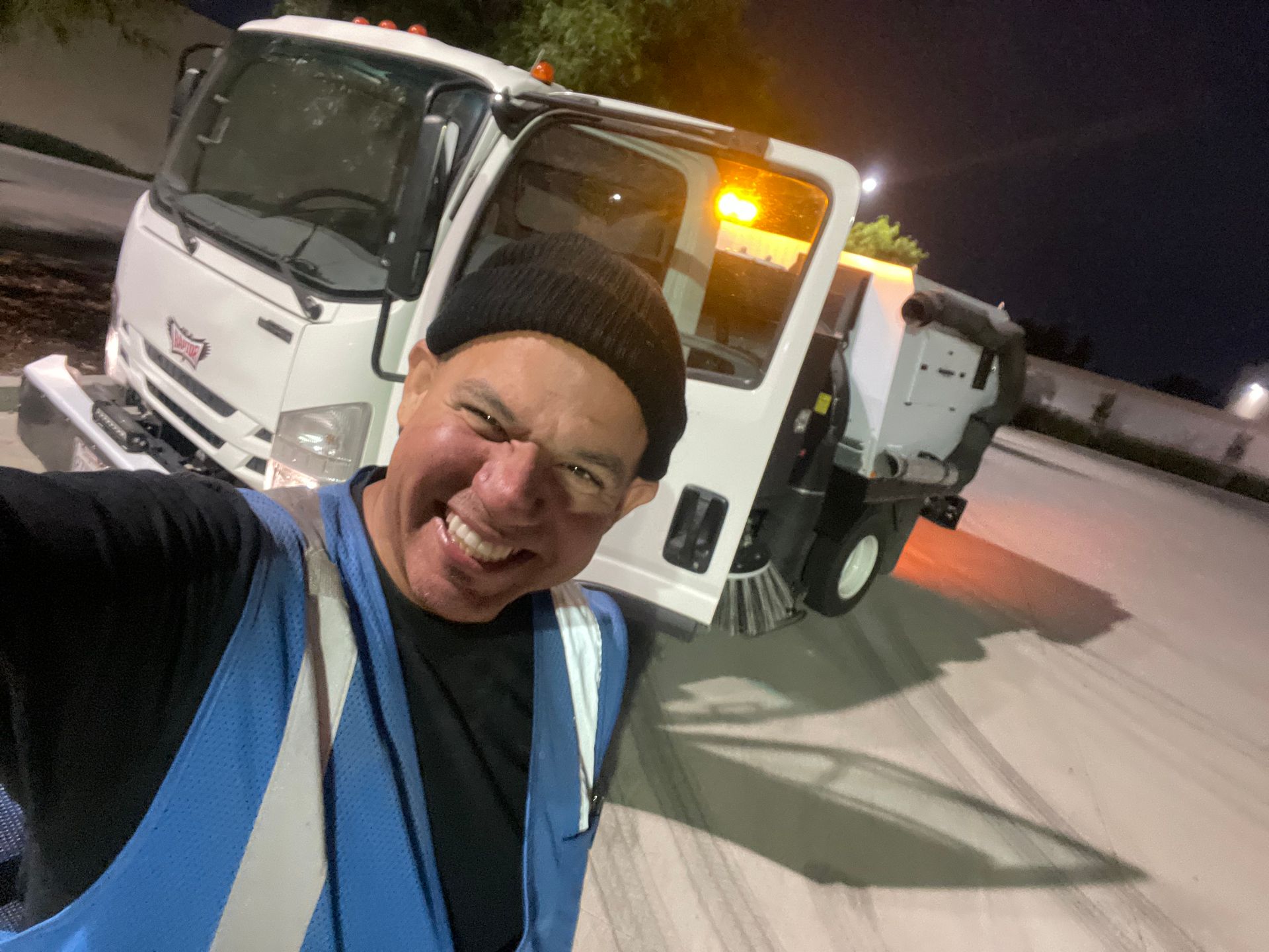 A man is taking a selfie in front of a street sweeper truck.