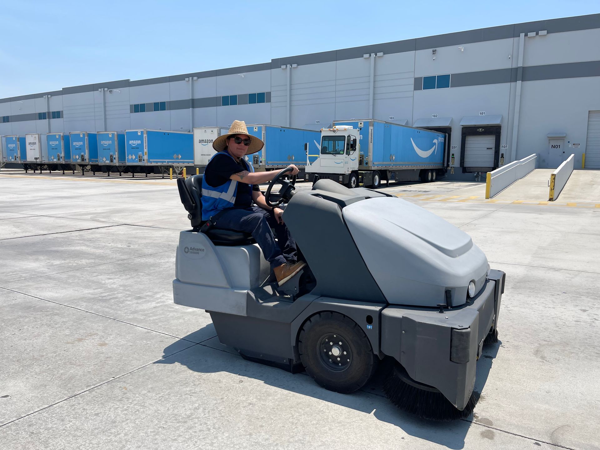 A man is driving a sweeper in front of a warehouse.