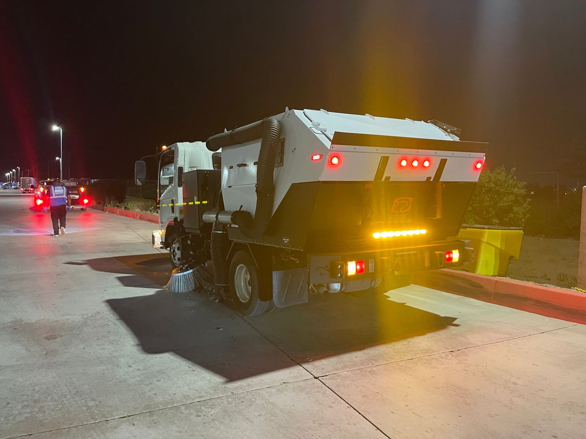 A trash truck is parked on the side of the road at night.