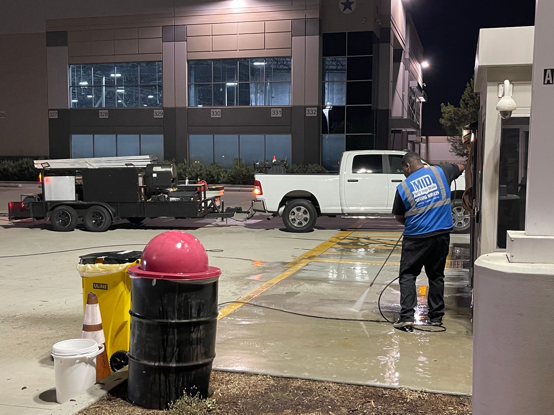A man in a blue vest is cleaning a parking lot at night