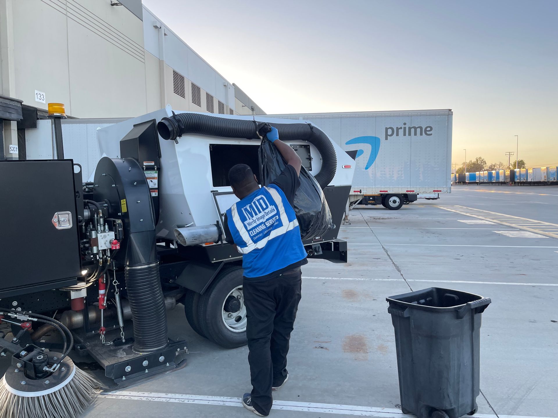A man is standing next to a broom truck in a parking lot.